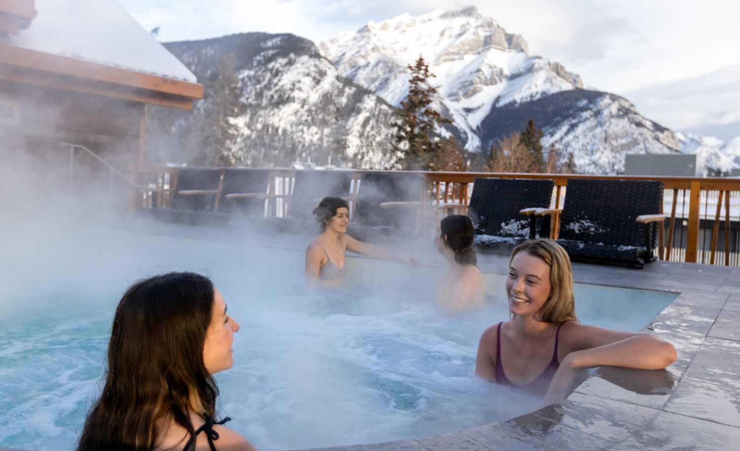 Four people in a rooftop hot tub with Cascade Mountain behind them in Banff National Park.